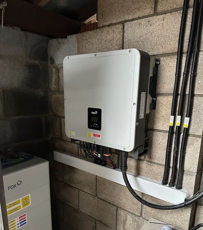 A FoxESS three-phase hybrid inverter and stacked battery modules mounted on a blockwork wall