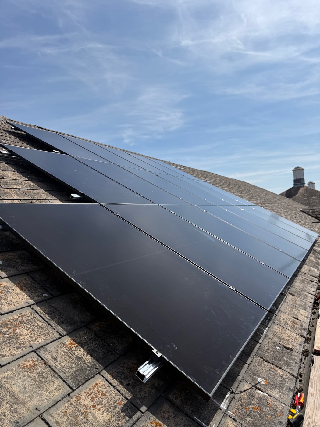Forty-four all-black panels running up a stone tiled roof under a blue sky