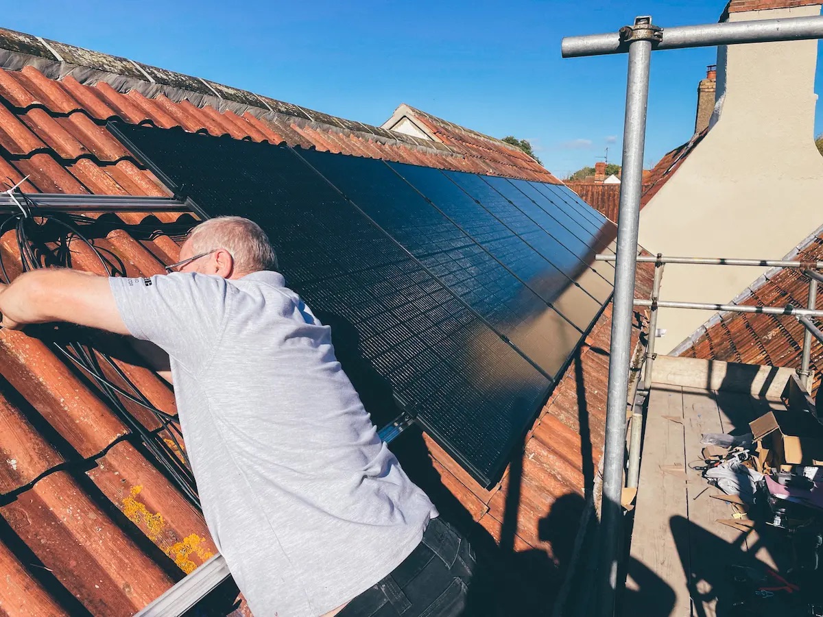Chris fitting all-black panels to a tiled roof from a scaffold on a bright day