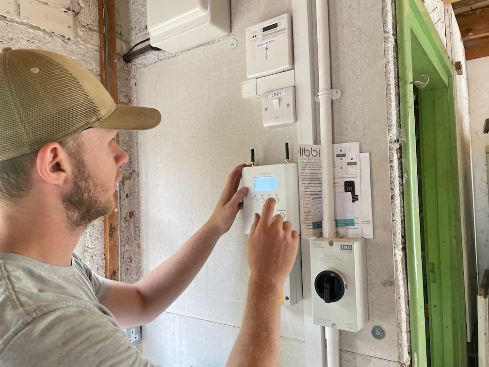 One of the team setting up a myenergi Libbi battery controller on a garage wall beside the generation meter